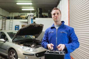 Portrait of male mechanic carrying car battery in workshop
