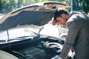 Young man looking under the hood of breakdown car