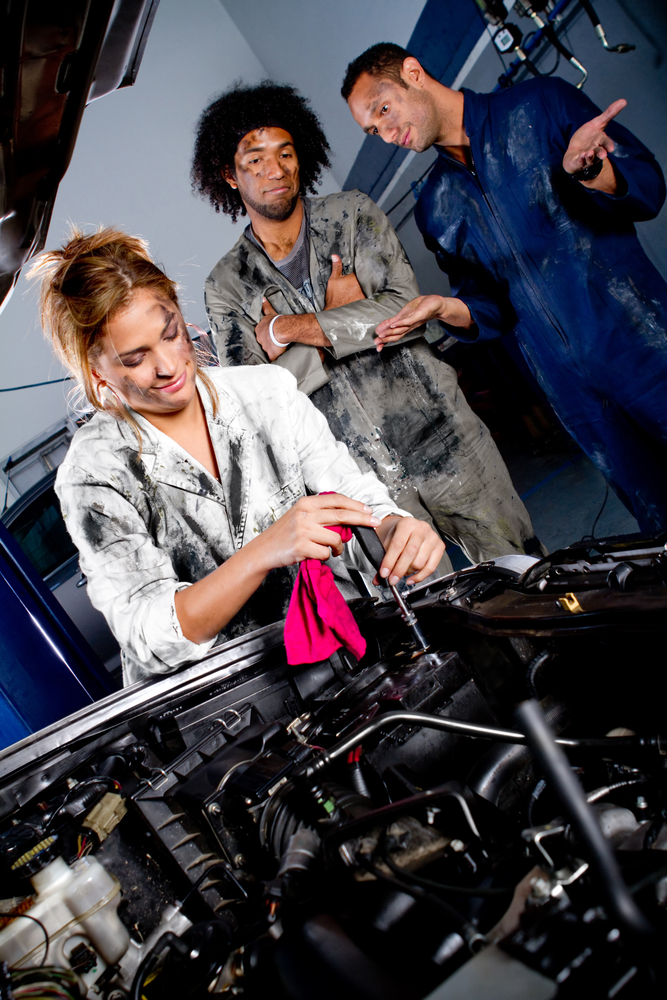 Female mechanic working on the hood of a car while colleagues watch